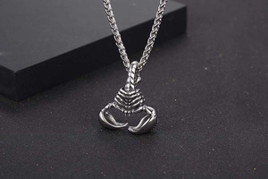 Detailed close-up of a silver-tone scorpion pendant with textured wheat chain on black base