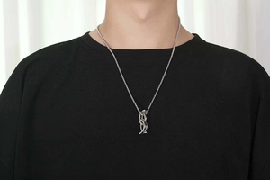 Close-up of a silver box chain necklace with a vertical overlapping letter logo pendant