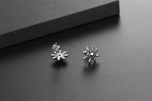 Macro shot of silver sunflower stud earrings with zircon on a textured background