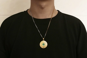 Detail of dual-tone titanium necklace featuring a gold hexagram pendant with green stone