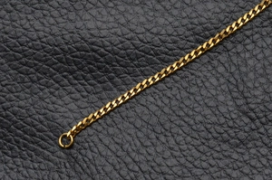 Détail macro d'une chaîne gourmette dorée polie sur un support en cuir de luxe