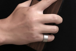 Close-up of wide titanium steel ring with textured rock finish on finger
