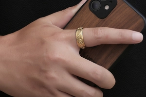 Close-up of golden Viking Celtic knot relief ring on finger with wood background