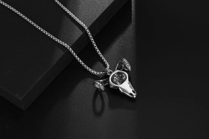 Macro shot of silver steel ram skull pendant with horns and cross chain on black surface