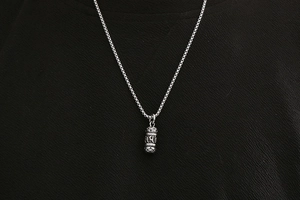 Detailed view of vintage silver steel cylinder pendant with engraved mantra symbols