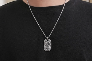 Macro detail of men's vintage dragon pendant on square link chain worn by a model