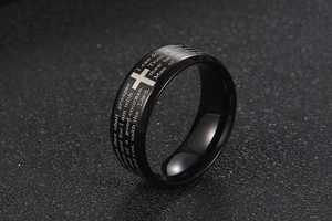 Macro detail of black stainless steel ring featuring silver cross and engraved scripture