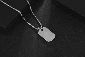 Close-up of brushed silver titanium dog tag pendant with elegant box chain on dark base