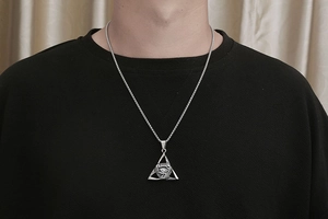 Detail of vintage triangular evil eye pendant on a silver chain worn by a male model