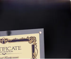 Close-up of clear acrylic certificate frame with gold metal bolts on a black background