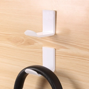 Detail view of two white L-shaped adhesive headphone hooks mounted on a light wood surface