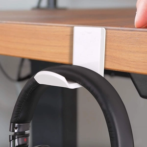 Minimalist white under-desk headphone holder hook mounting a black headset on wood desk
