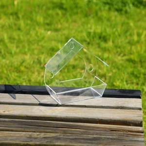 Transparent acrylic house-shaped bird feeder on a wooden bench with natural outdoor garden background