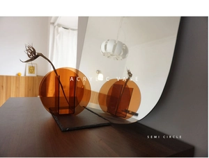 Detail of amber acrylic semi-circle vase on wooden table with mirror reflections
