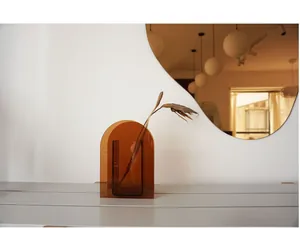 Close-up of amber acrylic arch vase with dry branches on a grey textured surface