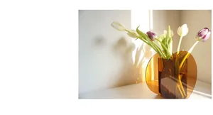 Detail of modern amber acrylic geometric vase with colorful tulips and artistic shadows