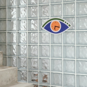 Modern acrylic Evil Eye wall clock with green eyelid and orange dial on glass wall