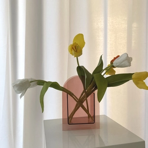 Vase aus rosa Acryl im Bogendesign mit Tulpen vor einem weichen Vorhang im Innenraum