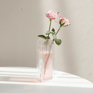 Minimalist acrylic ripple vase with rainbow finish and pink roses on a white desk