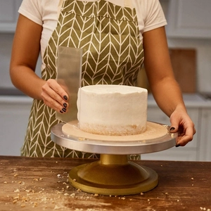 Transparent acrylic cake scraper smoothing white cream on a metal revolving stand