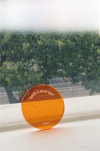 Detail of orange translucent acrylic coaster with white HAVE A NICE DAY printed text