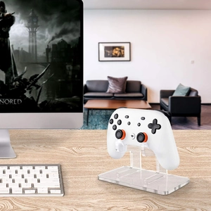 Clear acrylic game controller stand holding a white gamepad on a wooden desktop setup