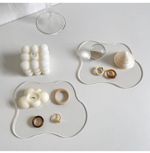 Irregular wave-shaped acrylic trays holding jewelry and candles in a minimalist scene