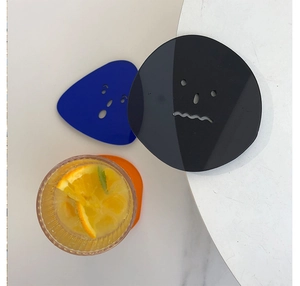 Close-up of colorful acrylic coasters with hollow face designs and a glass of water