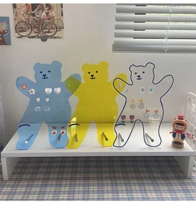 Three bear-shaped acrylic earring organizers in blue and yellow on a blue checkered cloth