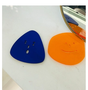 Detail of blue and orange acrylic coasters with smiley cutouts on a marble surface