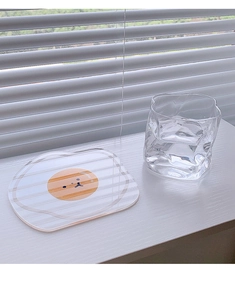 Detail of transparent acrylic coaster with fried egg cartoon and textured glass cup