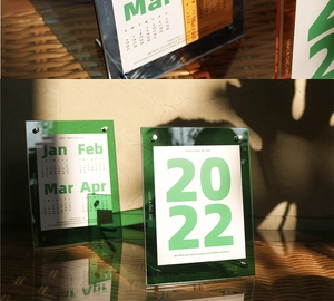 Detail van donkergroene acryl bureaukalender frame met metalen bouten en kalenderkaarten