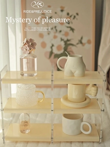 Cosmetics and ceramic mugs displayed on a clear two-tier acrylic organizer shelf