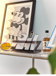 Detalle de organizador de escritorio de acrílico gris con niveles para mandos y móviles
