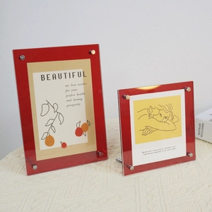 Detail of red transparent acrylic photo frames with metal screw fixings on a textured cloth