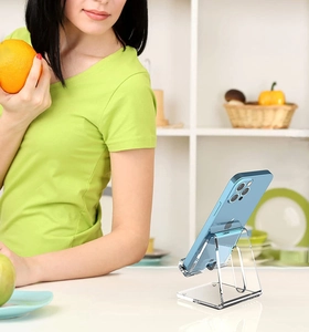 Clear acrylic phone stand displayed in a kitchen setting holding a blue smartphone