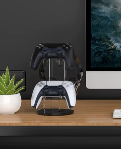 Vertical acrylic gaming stand holding two controllers and a black headset on a desk