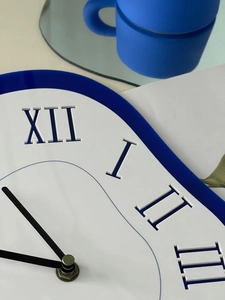 Detail of white matte wall clock featuring Roman numerals and blue frame for modern home decor