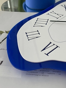 Detail of melting wall clock with Roman numerals on blue and white acrylic frame