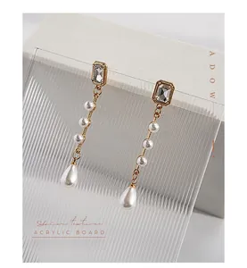 Close-up of vintage long pearl drop earrings hanging on a wavy acrylic texture board