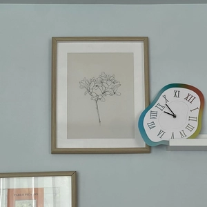 Melting wall clock with Roman numerals and rainbow frame on a blue living room wall