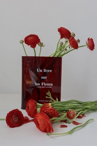 Close-up of a red translucent acrylic book vase with white floral text and fresh flowers