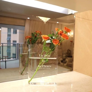 Clear acrylic book flower vase with orange roses on marble tabletop home decor