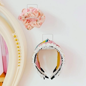 Support acrylique montrant un chouchou pêche rose et un serre-tête à perles sur un mur