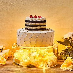 Clear acrylic cake stand filled with yellow flowers and warm LED lights for wedding events