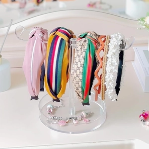 Clear acrylic headband holder with six diverse colorful hairbands on a light desk
