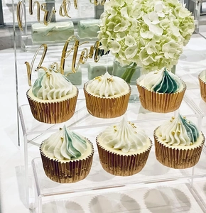 Clear acrylic tiered stand displaying golden cupcake liners for wedding party decor