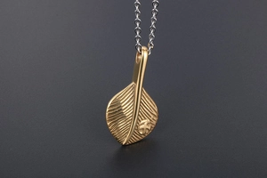 Detail of golden feather pendant with intricate leaf veins and small bird logo on silver chain
