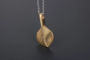 Macro detail of golden feather pendant with textured patterns on a vintage steel necklace