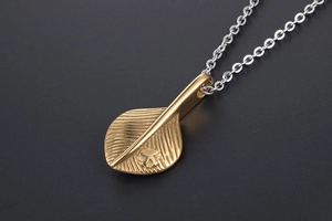 Macro shot of gold feather pendant with detailed leaf veins on a silver link chain
